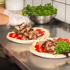 Ręce w rękawiczkach układają mięso na plackach z pomidorami i natką. Pyszny gemuse kebab gotowy do podania.