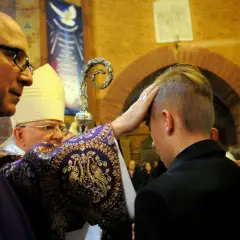 Biskup udziela sakramentu bierzmowania młodemu mężczyźnie. To ważny moment w jego drodze wiary, wybiera imienia do bierzmowania męskie.