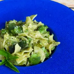 Pyszny makaron z bobem i cukinią, posypany parmezanem, podany na niebieskim talerzu.