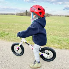 Kind mit rotem Helm übt das laufrad fahren auf einem Feldweg.