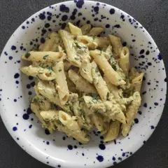 Penne z kremowym sosem, kawałkami tuńczyka i zieloną natką pietruszki, podane w talerzu w granatowe cętki.