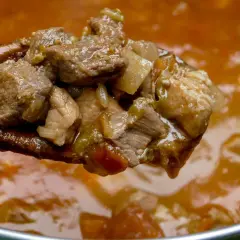 Gulasz wieprzowy na drewnianej łyżce. Kiedy solić mięso wieprzowe na gulasz? Najlepiej na początku, by wydobyć smak.