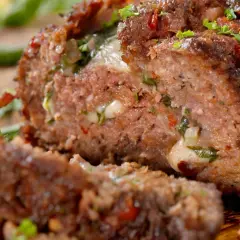 Un succulento polpettone ripieno, con formaggio filante e erbe aromatiche, pronto per essere gustato.