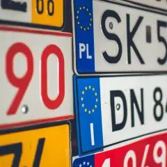 Zbliżenie na stos tablice rejestracyjne państw. Widać numery i litery, m.in. PL, SK, DN.