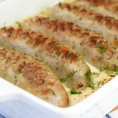 Biała kiełbasa w sosie chrzanowo-musztardowym, zapieczona w naczyniu, ozdobiona koperkiem. Pyszne danie gotowe do podania.