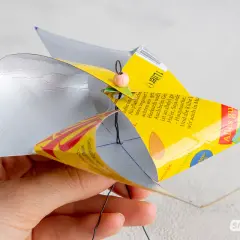 Bastelanleitung für ein Windrad: Eine Hand hält ein selbstgemachtes Windrad aus einer Getränkeverpackung, das sich dreht. Eine Vorlage zum Windrad basteln ist hier zu sehen.