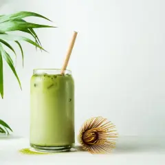 Orzeźwiające matcha latte z lodem i bambusową słomką, obok bambusowa miotełka. Poznaj niezwykłe matcha właściwości!