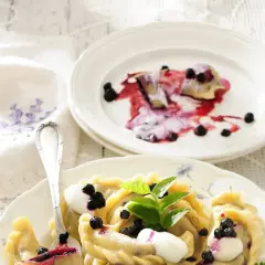 Pyszne pierogi z jagodami, polane śmietaną i posypane świeżymi owocami. Idealne na letni deser.
