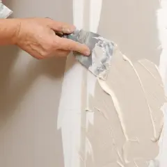 Mano stende stucco su una giuntura di cartongesso, ricordando che il cartongesso ha un verso.