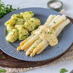 Spargel mit Sauce Hollandaise und Petersilienkartoffeln, garniert mit frischer Petersilie und einer Zitronenspalte. Ein Klassiker der deutschen Küche.