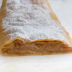 Ein köstlicher Apfelstrudel mit fertigem Strudelteig, bestäubt mit Puderzucker. Daneben liegen frische Apfelstücke.