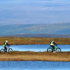 Två cyklister njuter av en cykelsemester i Sverige, susar fram längs sjöar i ett vidsträckt landskap.