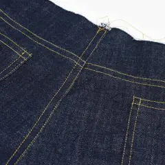 Close-up of the yoke on dark blue jeans, showing yellow stitching and raw edges.