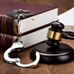Kajdanki, młotek sędziowski i księgi prawne na drewnianym stole.