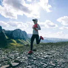 Une coureuse s'élance sur un sentier rocailleux, dominant des montagnes majestueuses. Un paysage digne d'un trail mythique en France.