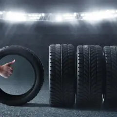 Opona całoroczna z kciukiem w górę obok rzędu opon na tle stadionu.