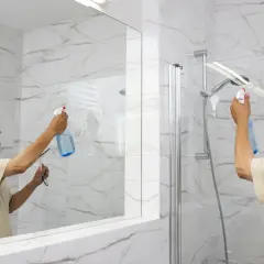 Un homme nettoie la porte de douche en verre pour enlever le calcaire.