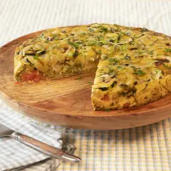 Pastel de acelgas con verduras y queso gratinado, servido en plato de madera.