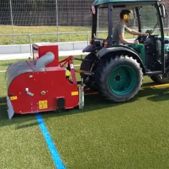 Traktor mit Anbaugerät reinigt Kunstrasen.