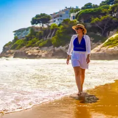 Kobieta w słomkowym kapeluszu spaceruje po plaży. Idealne miejsce na tanie loty na majówkę, by poczuć słońce i fale.