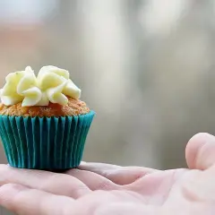 En hand håller en saftig muffins med vit frosting.