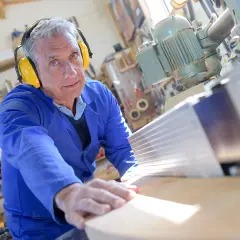 Ein Mann in Schutzkleidung arbeitet an einer Holzbearbeitungsmaschine. Seine Erfahrung im Handwerk spiegelt sich in seinen **altersteilzeit erfahrungsberichte** wider.