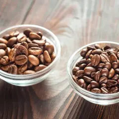 Dwie miseczki z ziarnami kawy: jedna z jaśniejszymi ziarnami arabiki, druga z ciemniejszymi, tworzącymi idealną mieszankę arabica i robusta.
