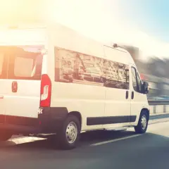 Biały bus do Niemiec pędzi autostradą w słoneczny dzień.