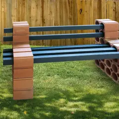 Eine rustikale Gartenbank, die man leicht selber bauen kann, mit Sitzflächen aus dunklen Balken und Stützen aus Ziegelsteinen.