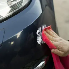 Ręka z czerwoną mikrofibrą poleruje lakier samochodu, usuwając drobne rysy. Czy powłoka ceramiczna wady i zalety są warte tej pracy?