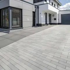 Moderne Einfahrt pflastern mit grauen Steinen. Das Haus hat eine graue Fassade und weiße Akzente.