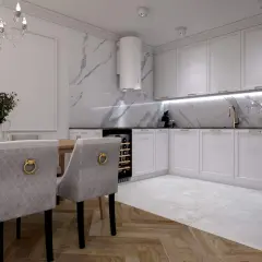 Elegancka kuchnia z białymi frontami, okap tuba nad blatem z marmurowym wzorem. Aranżacje stołu z krzesłami tworzą przytulną jadalnię.
