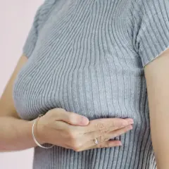 Kobieta bada swój sutek, odczuwając pieczenie. Dba o swoje zdrowie.