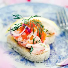 En läcker toast Skagen med räkor, rom, dill och rödlök på en blåvit tallrik.