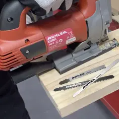 Lames pour reconnaître lame scie sauteuse métal. Une scie sauteuse rouge WAHLEN et trois lames sont posées sur une planche de bois.