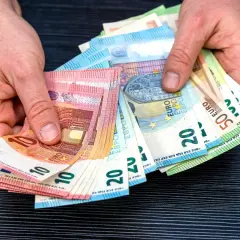 Dłonie trzymają plik banknotów euro, które są walutą w Hiszpanii. Widoczne nominały to 10, 20 i 50 euro.
