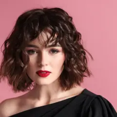 Kobieta z falowanymi włosami w stylu botticelli bob, z wyrazistymi czerwonymi ustami, na różowym tle.