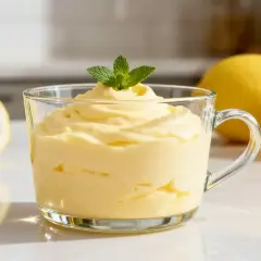 Morbida mousse al limone in una tazza di vetro, guarnita con menta fresca. Limoni interi e tagliati sullo sfondo.