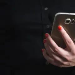 Dłoń z czerwonymi paznokciami trzyma telefon, szukając informacji, jak zablokować SMS premium.