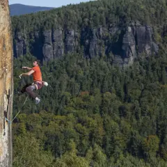 Ein Mann klettert an einer Felswand in Tschechien. Im Hintergrund erstreckt sich ein dichter, grüner Wald.