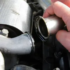 Dłoń trzymająca metalową rurkę z widocznymi śladami oleju, część układu dolotowego turbiny auto.