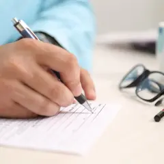 Dłoń pisze na formularzu, obok okulary i kubek. Zastanawiasz się, na co zwrócić uwagę przy kredycie hipotecznym?
