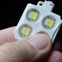 Moduł z czterema diodami LED, trzymany w dłoni, gotowy do podłączenia do włącznika światła.