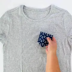 A hand holds a navy fabric with white anchors, demonstrating how to sew front pockets on pants.