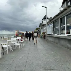 Spacer w Sarbinowie, gdy pada. Ludzie idą promenadą obok barów z lodami i kawiarni, szukając atrakcji.