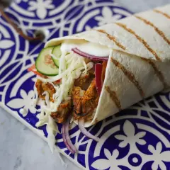 Domowy kebab zawinięty w tortillę z warzywami i sosem na ozdobnym talerzu.