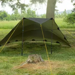 Zielony tarp rozstawiony na trawie, z żółtymi linkami. Pokazuje, jak zrobić namiot w prosty sposób, idealny na biwak.