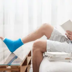 Mężczyzna z niebieskim gipsem na nodze czyta książkę, próbując zagłuszyć **uraz psychiczny** po wypadku.