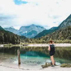 Frau mit Rucksack genießt den Blick auf einen türkisfarbenen See und die Berge. Perfekter Ort zum Wandern in Slowenien.