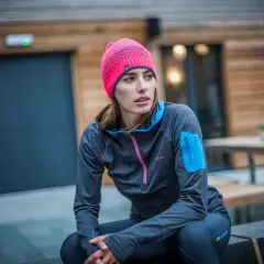 Kobieta w różowej czapce i sportowej bluzie siedzi na zewnątrz.